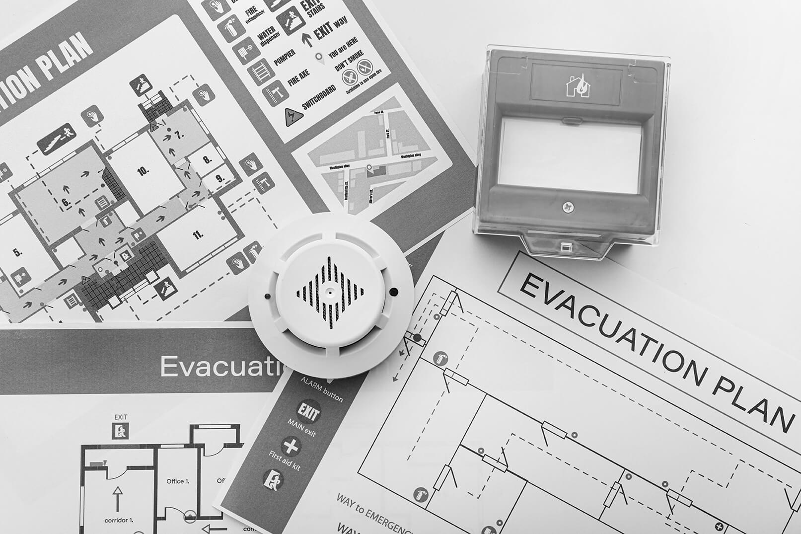 Evacuation plans, smoke detector and manual call point on white